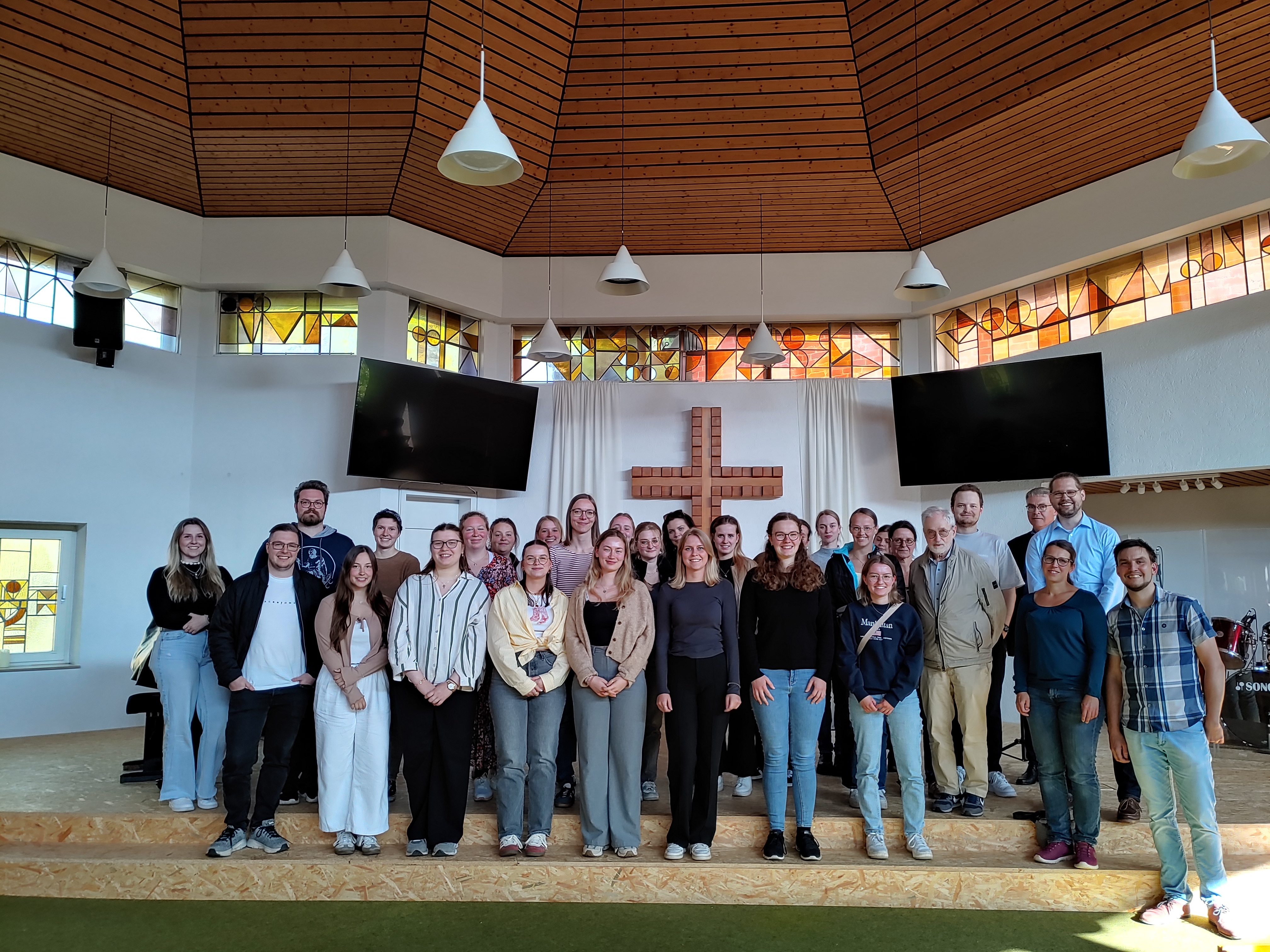 Die Teilnehmenden des Studientages 2025 stehen vor dem Altar in der Kirche der Baptistengemeinde Münster mit Pastorenpaar Enders!
 © Universität Osnabrück | Kathleen Burrey